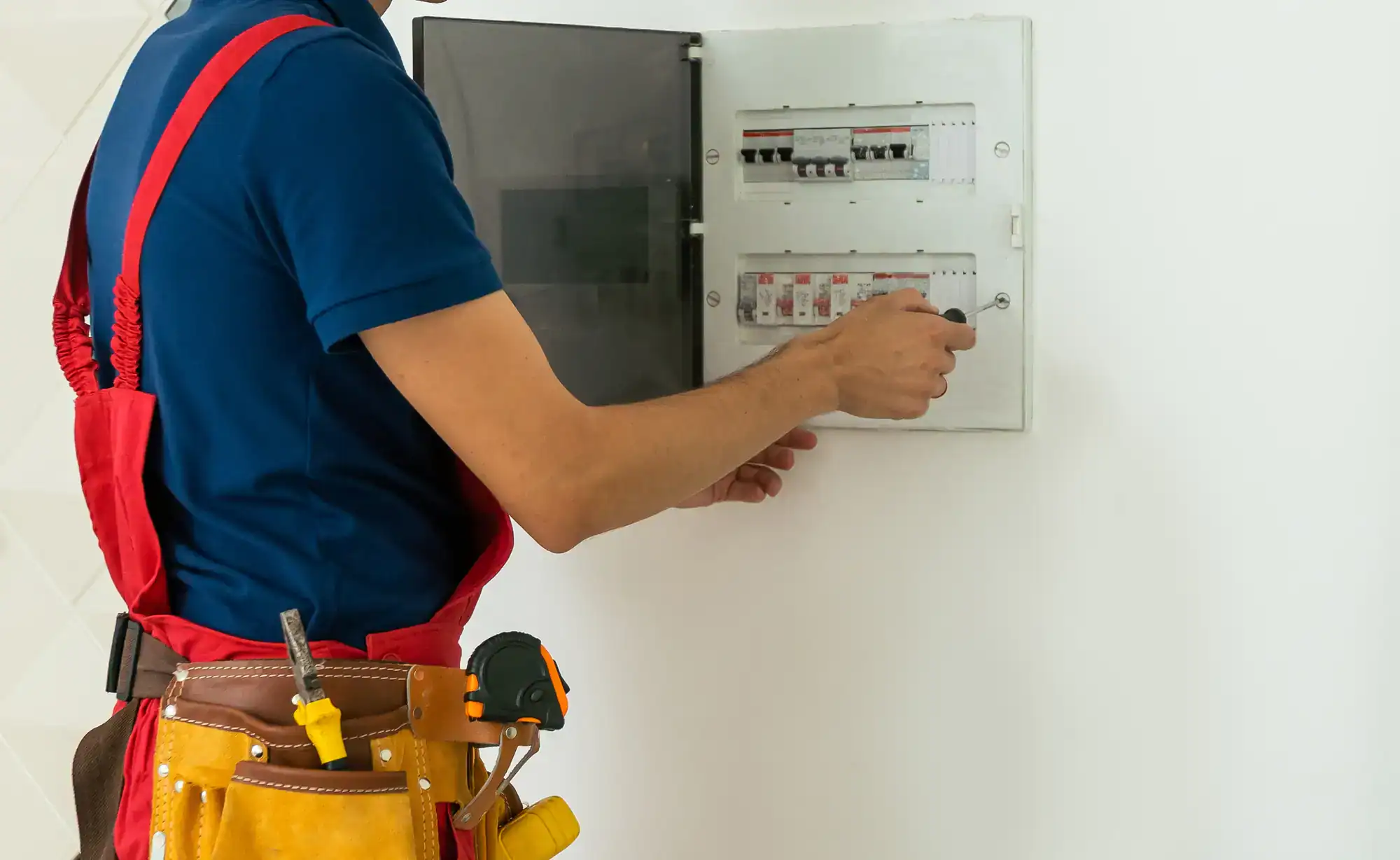 Electrician inspecting a fuse box in a residential home, wearing safety gloves and using tools in Dallas County, Texas